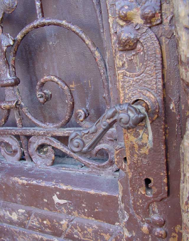 Ozdobna klamka do drzwi wejściowych kamienicy na ul. Wyspiańskiego. Precyzyjny odlew staliwny. W tle fragment kutej kraty.(zdjęcie pozakonkursowe)