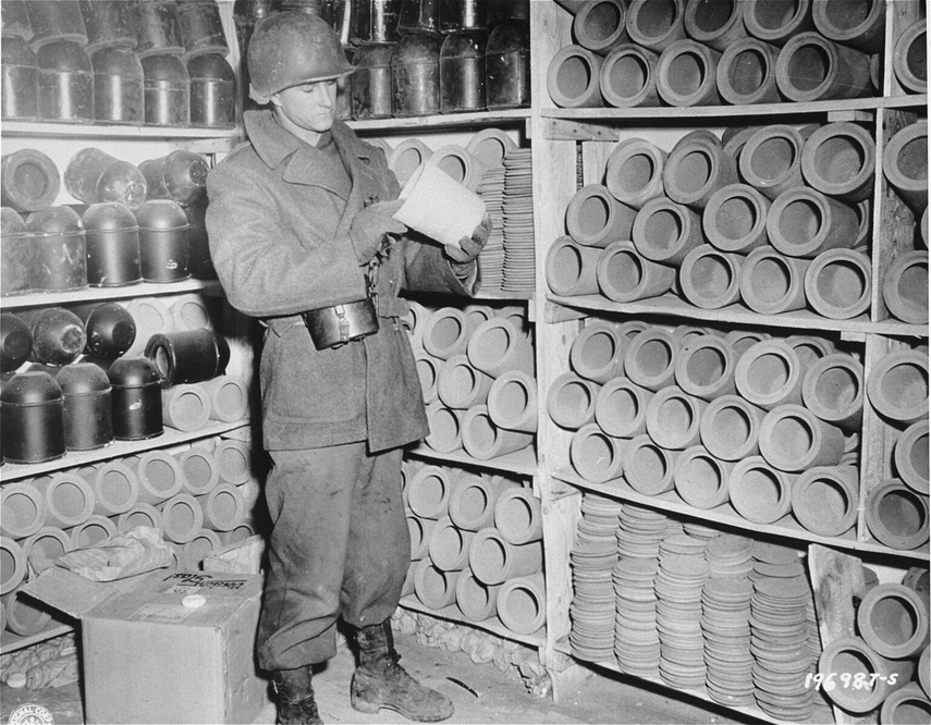 Elbląg, Amerykański żołnierz ogląda metalowe urny na prochy po wyzwoleniu obozu Natzweiler-Struthof. Z lewej strony na dole widoczne krążki szamotowe. Zbiory USHMM w Waszyngtonie